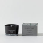Black candle labeled 'Hidden Forest' by Palmoire next to its packaging on a white background