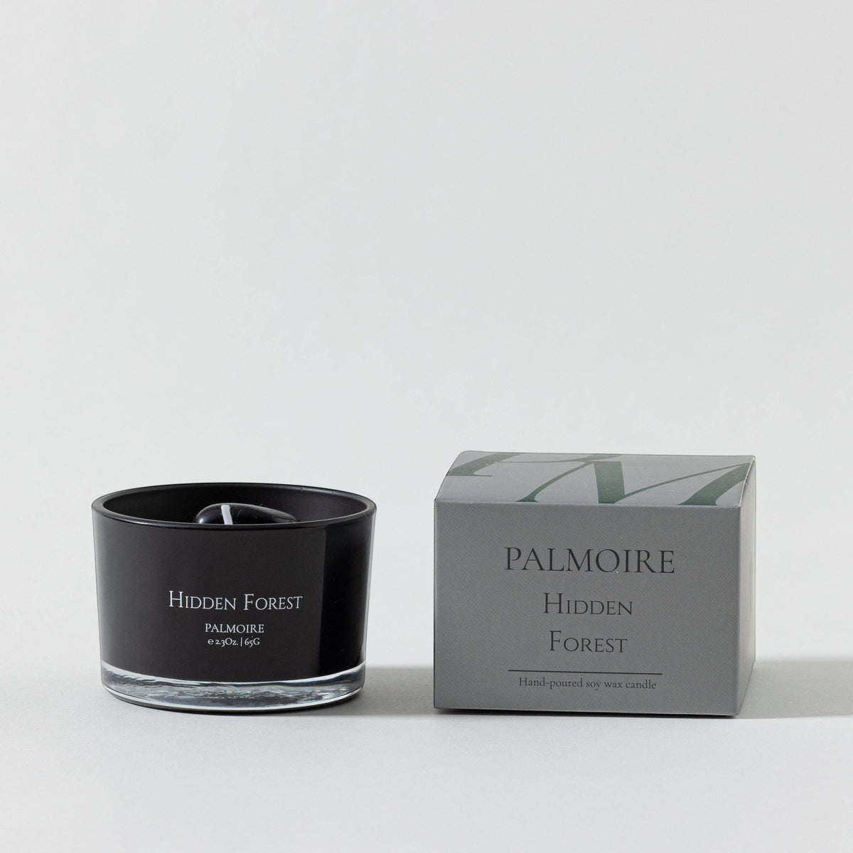 Black candle labeled 'Hidden Forest' by Palmoire next to its packaging on a white background