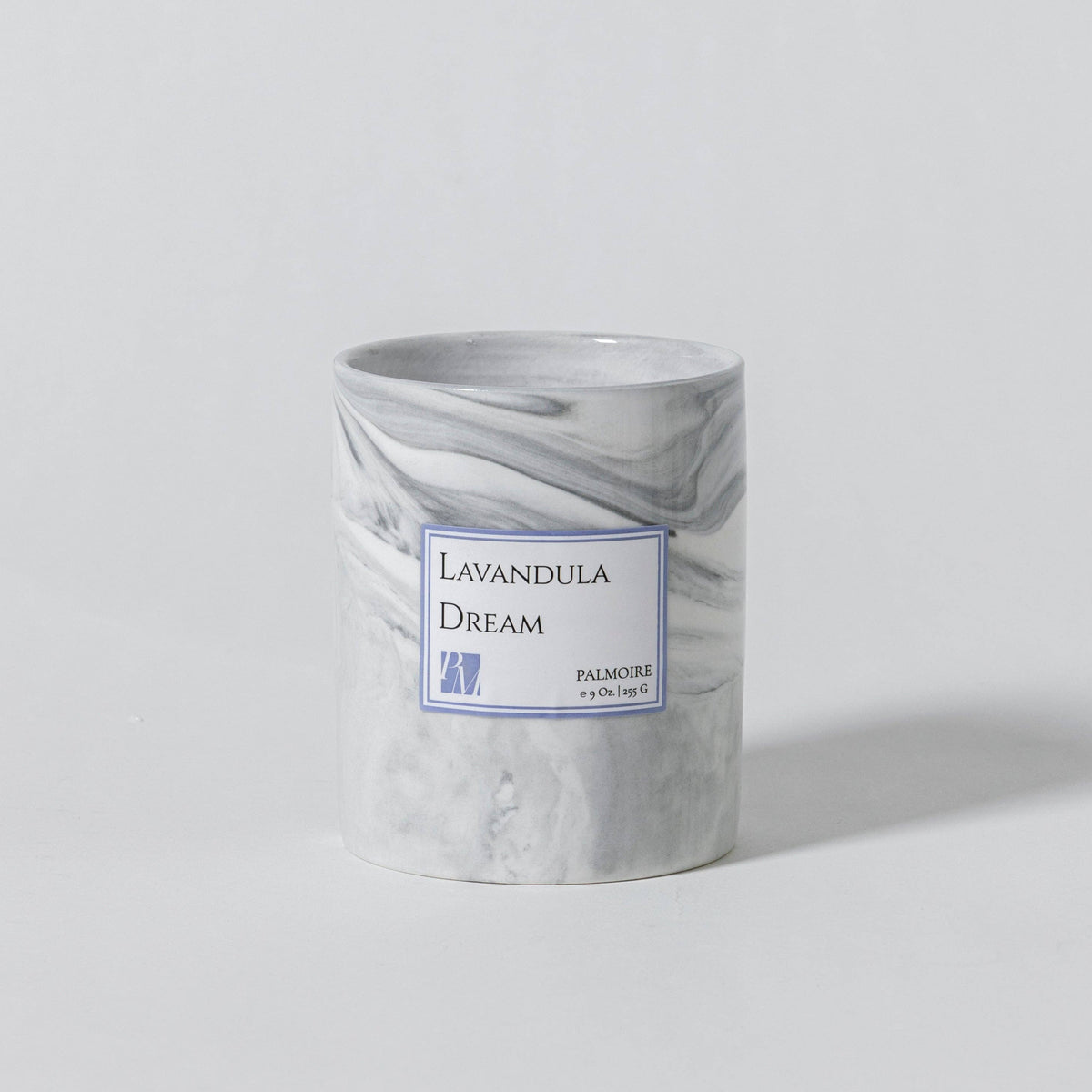 A cylindrical candle jar with a white and gray marble pattern, featuring a white label with blue borders that reads 'Lavandula Dream' and 'PAMAJI'.
