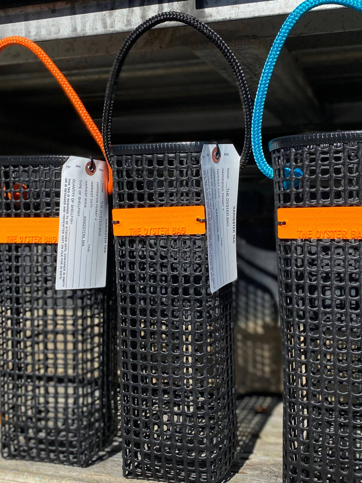 Three black woven bags with colorful straps hanging on a metal railing.