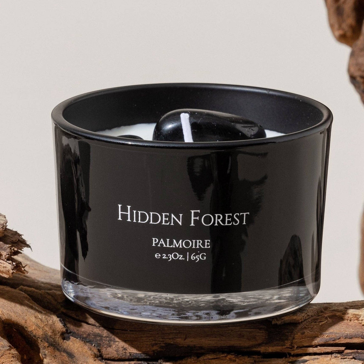 Black candle labeled 'Hidden Forest' on a piece of driftwood with a neutral background