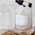 Glass container with ice cubes and a bottle labeled 'Snow Whisper' on a wooden surface.