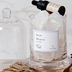 Glass container with ice cubes and a bottle labeled 'Snow Whisper' on a wooden surface.
