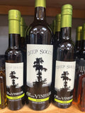 Three bottles of Deep South Oil and Vinegar Pizza Infused Olive Oil displayed on a wooden shelf, with the center bottle featured prominently and other bottles blurred in the background.