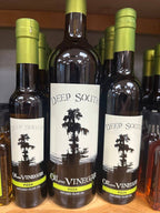 Three bottles of Deep South Oil and Vinegar Pizza Infused Olive Oil displayed on a wooden shelf, with the center bottle featured prominently and other bottles blurred in the background.