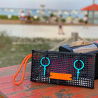 FULL MOOD The Clutch oyster bag in black mesh with bright orange rope handle and teal accents on a beach table