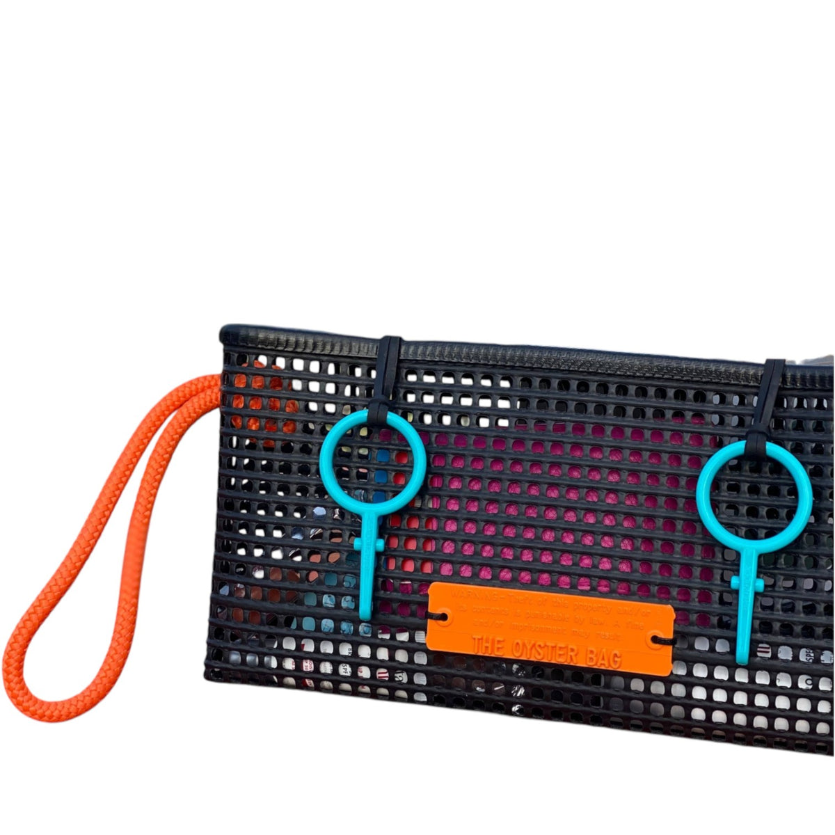 FULL MOOD The Clutch oyster bag in black mesh with bright orange rope handle and vibrant blue accents on a beach table