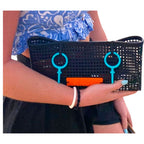 FULL MOOD black mesh clutch bag with teal circular accents held by a woman on a beach at sunset