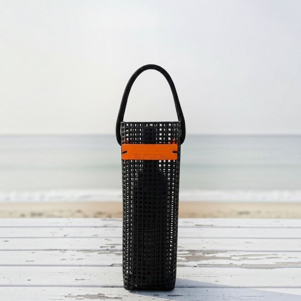 FULL MOOD black aquaculture mesh wine caddy with orange accent strap on a white wooden table at the beach