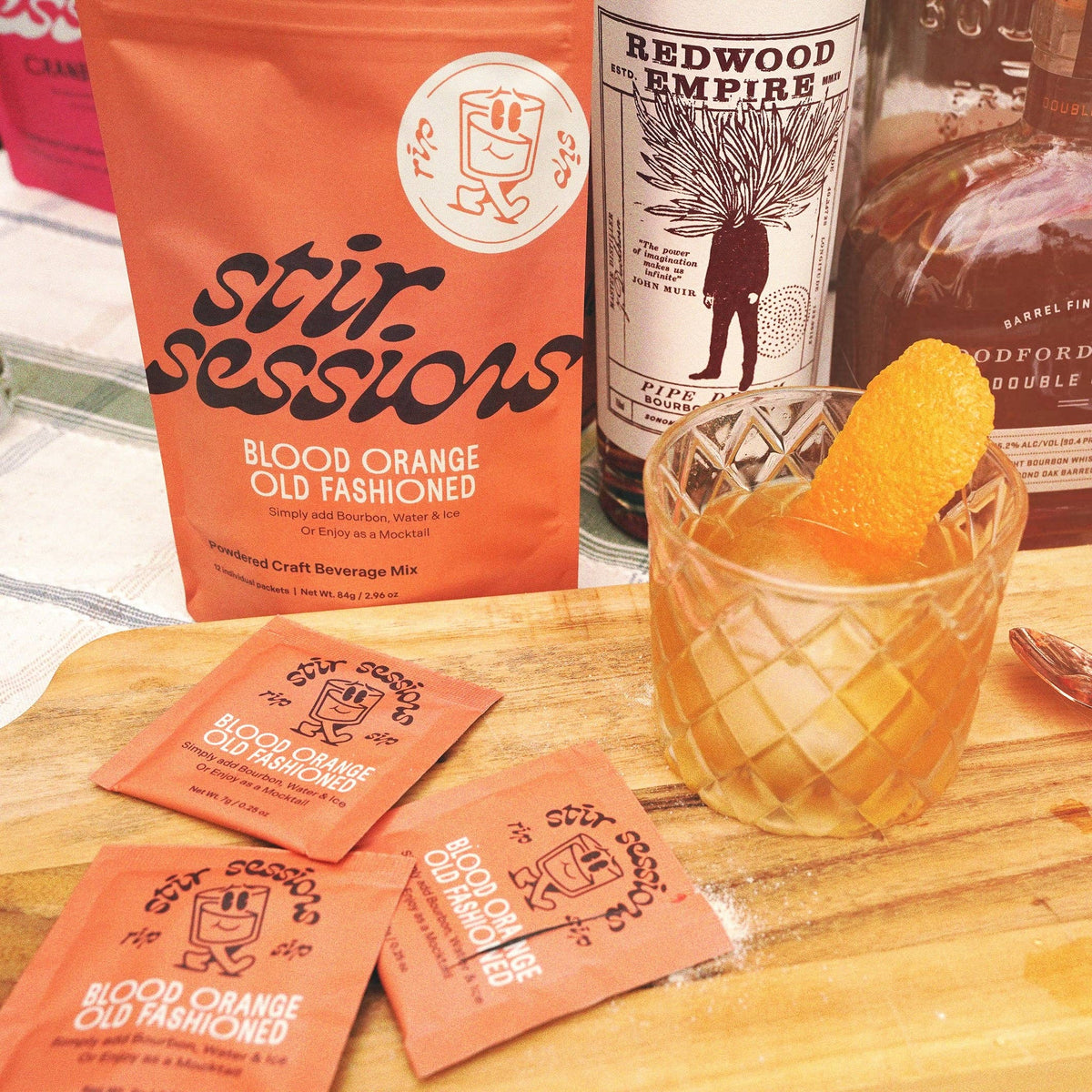 FULL MOOD Stir Sessions blood orange old fashioned cocktail mix packets and pouch with a prepared drink on a board