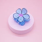 FULL MOOD blue daisy flower hair claw clip made of glossy acrylic with a pink center on a pink pedestal
