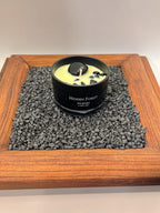 FULL MOOD Hidden Forest soy wax candle in a black jar with embedded gemstones, displayed on a bed of dark gravel.