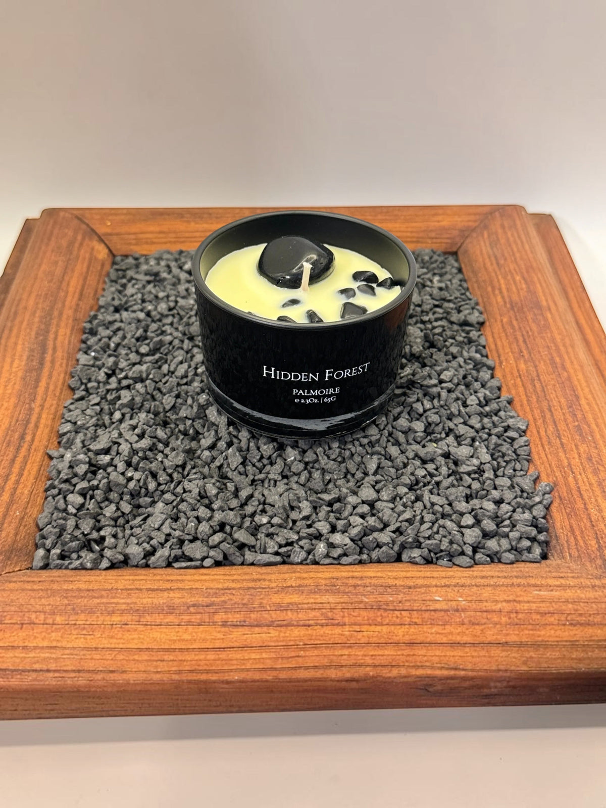 FULL MOOD Hidden Forest soy wax candle in a black jar with embedded gemstones, displayed on a bed of dark gravel.