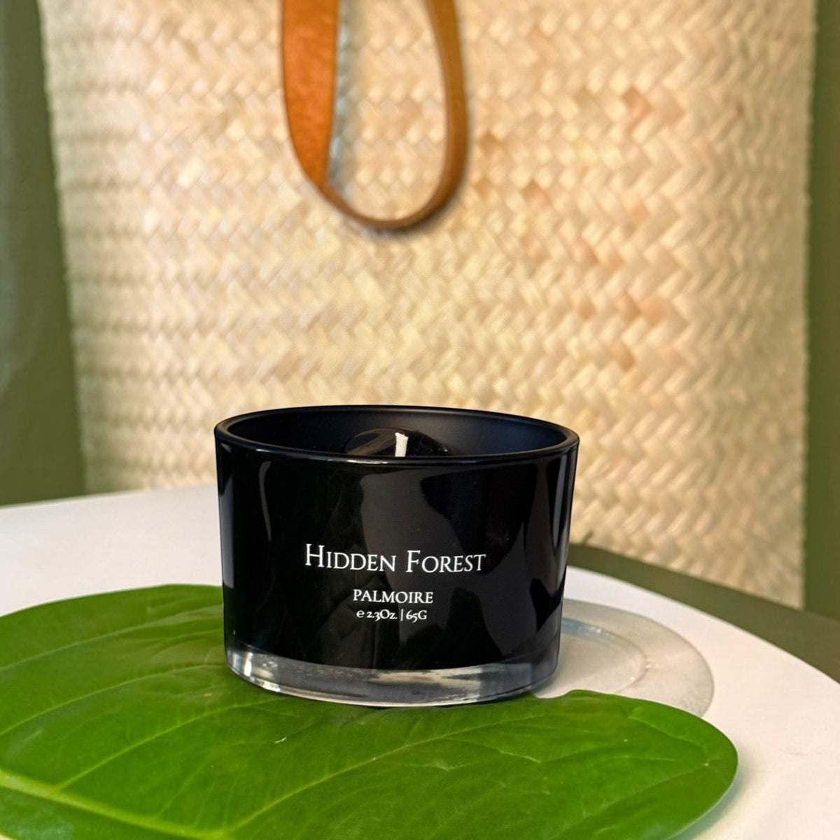 FULL MOOD Hidden Forest soy wax candle in a black glass jar with an embedded gemstone, resting on a large green leaf.
