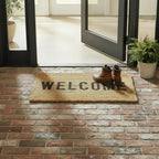 FULL MOOD woven jute doormat with black "WELCOME" lettering, placed on brick entryway with brown boots.