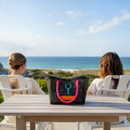 FULL MOOD Mini Market tote bag in black open-grid plastic with bright pink rope handles on a table by the ocean.