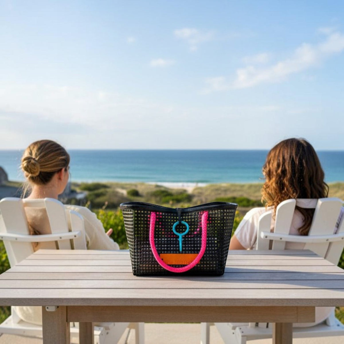 FULL MOOD Mini Market tote bag in black open-grid plastic with bright pink rope handles on a table by the ocean.