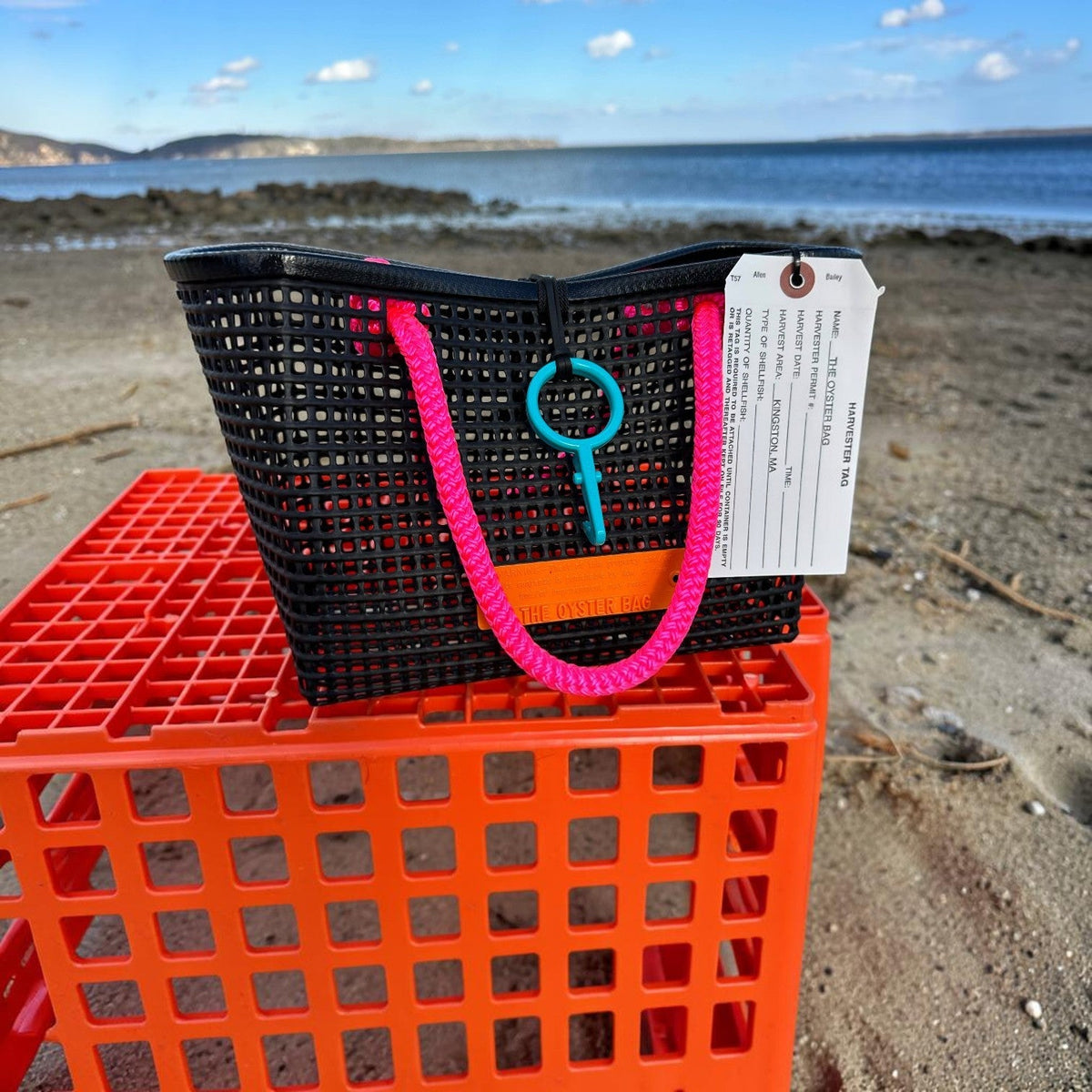 FULL MOOD Mini Market tote bag in black open-grid plastic with bright pink rope handles, sitting on an orange crate.