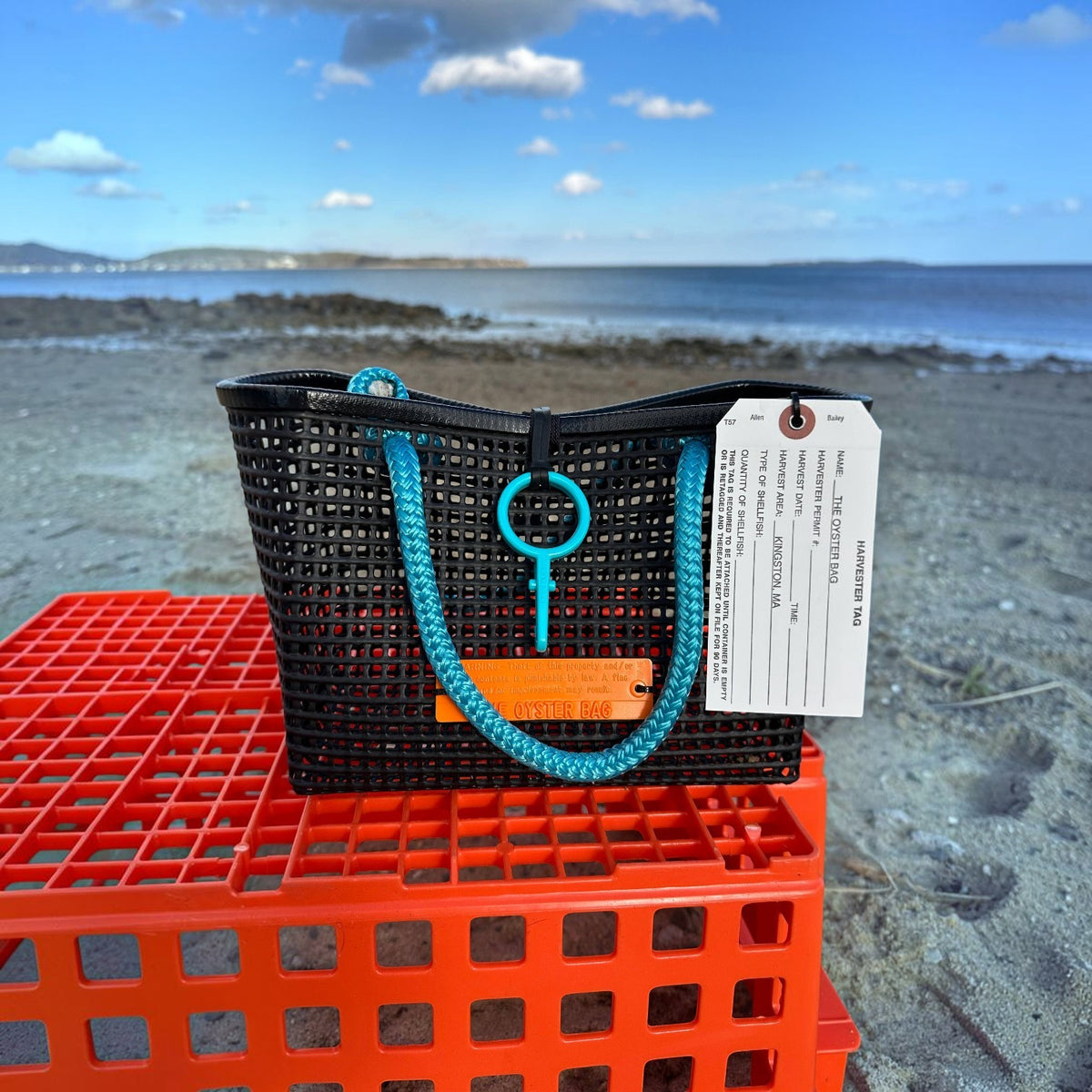 FULL MOOD Mini Market tote bag in black open-grid plastic with bright blue rope handles, set on an orange crate.