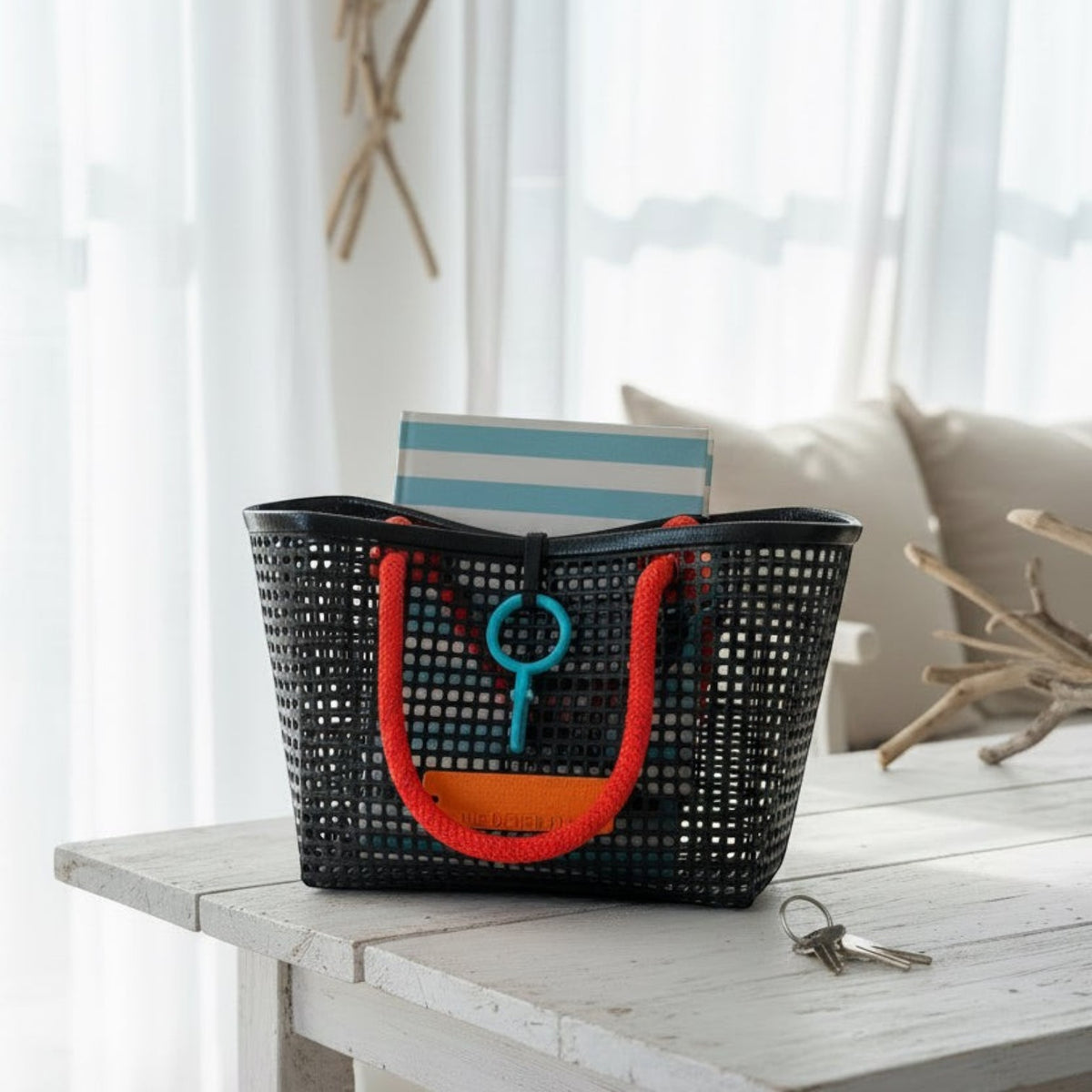 FULL MOOD Mini Market tote bag in black open-grid plastic with bright orange woven rope handles on a white table.