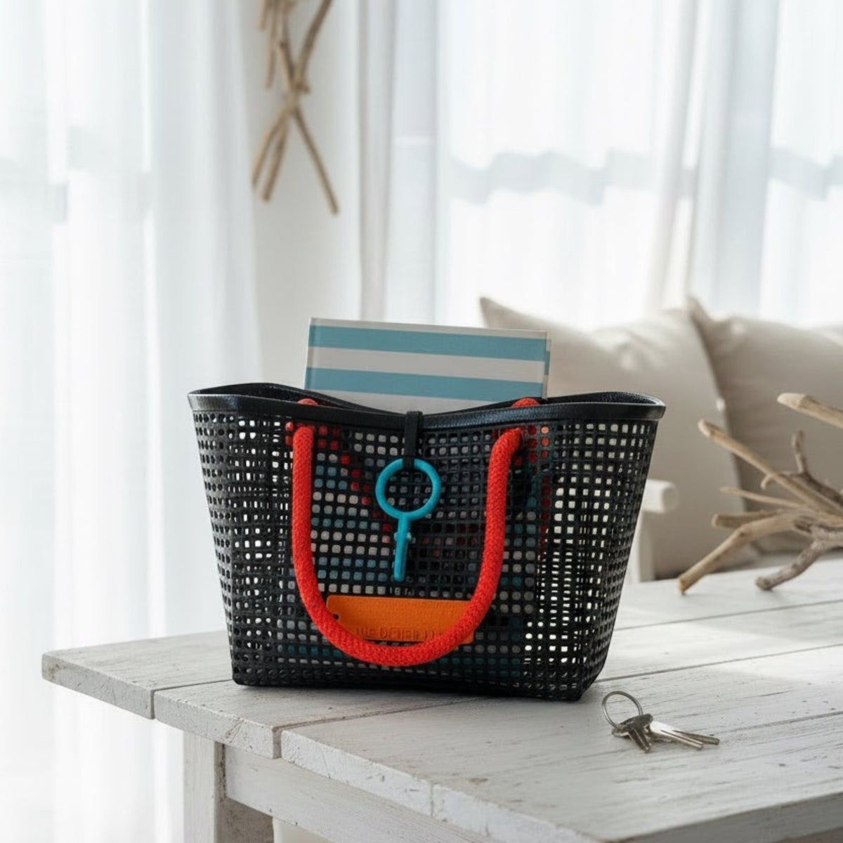 FULL MOOD Mini Market tote bag in black open-grid plastic with bright orange rope handles on a rustic white table.