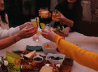 FULL MOOD Stir Sessions Pina Colada cocktail mix packet on a table with friends sharing drinks and a charcuterie board