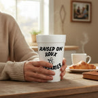 FULL MOOD 20oz white styrofoam cup with Raised on Roux & Rosaries text held by hands on a wooden table.