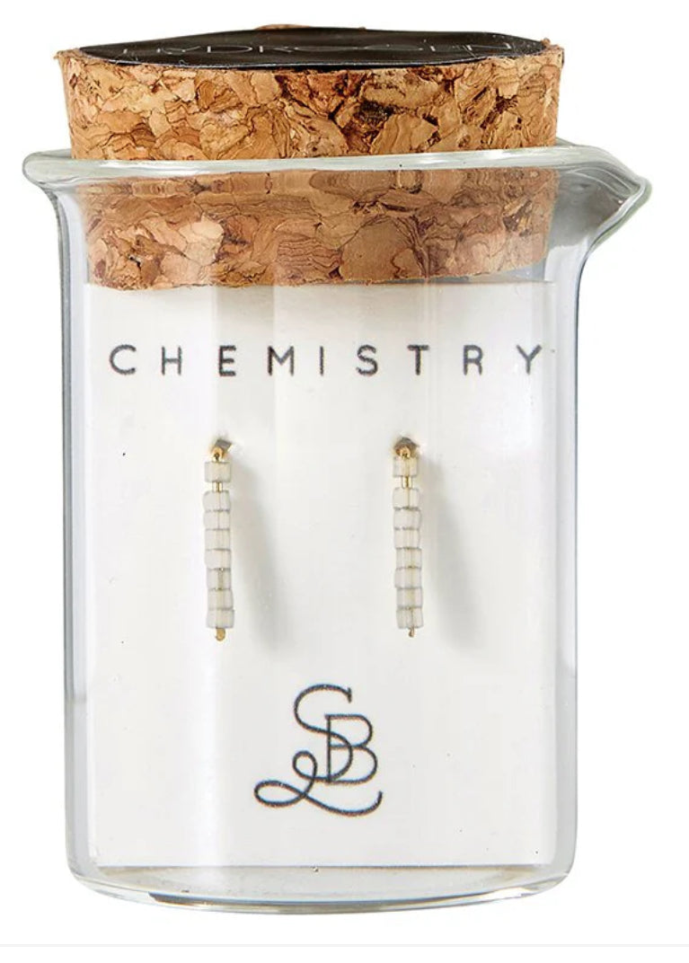 Glass jar with cork lid containing earrings and 'Chemistry' text, on a white background