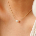 Pearl necklace on a person wearing a brown top and white cardigan
