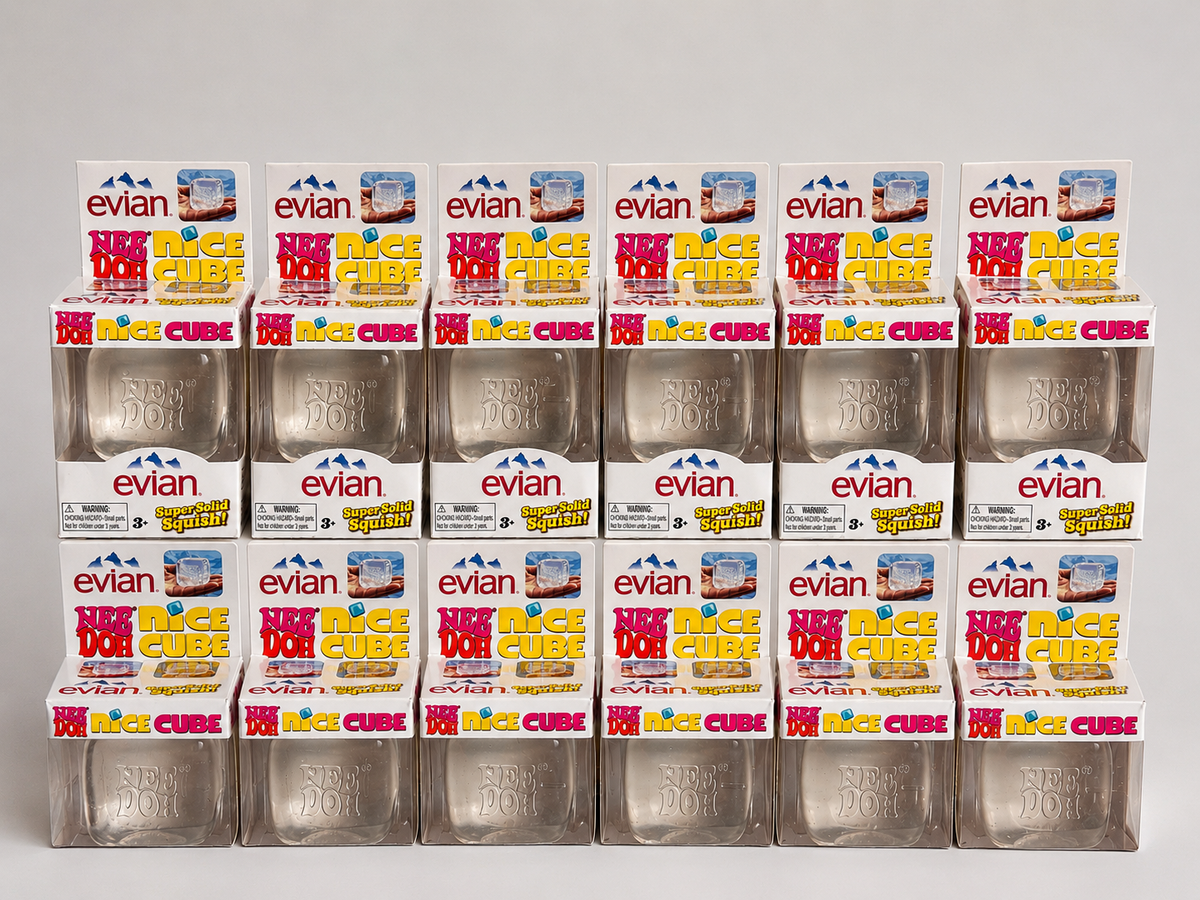 A 15-pack of Evian Magic Cube bath salts in clear plastic tubs with white and colorful retail boxes on top, arranged in a grid on a light gray background.
