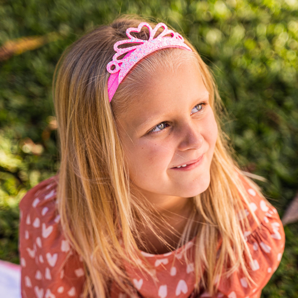 Young girl wearing a pink tiara with a blurred green background