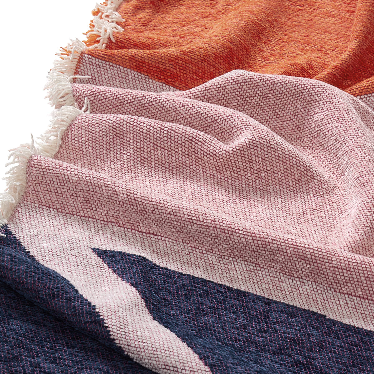 A close-up of a woven textile with fringed edges, showing a soft pink section layered over a dark navy section with a light beige diagonal stripe, and part of an orange section visible at the top.