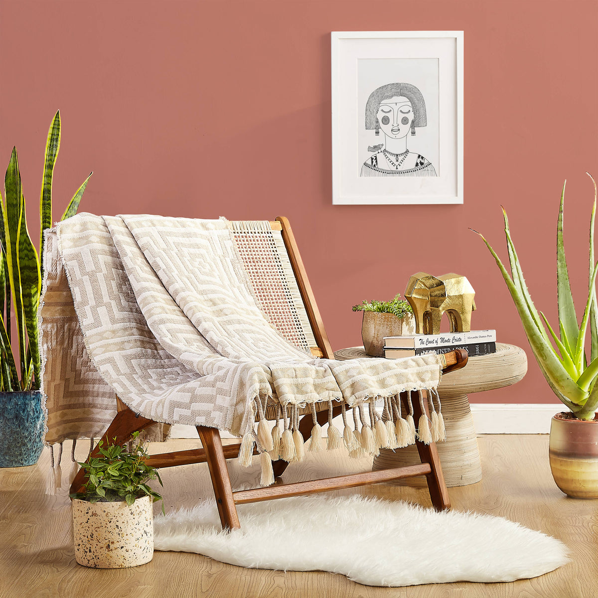 Wooden chair with a patterned throw blanket in a room with plants and a framed picture on the wall.